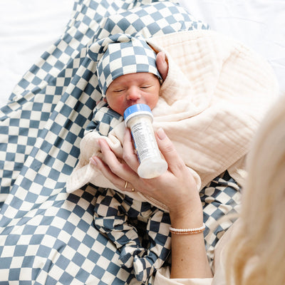 newborn baby wearing the miles collection while being fed a bottle by women