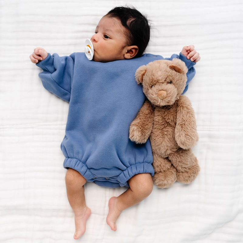 cadet sweatshirt romper baby boy laying on bed with teddy bear