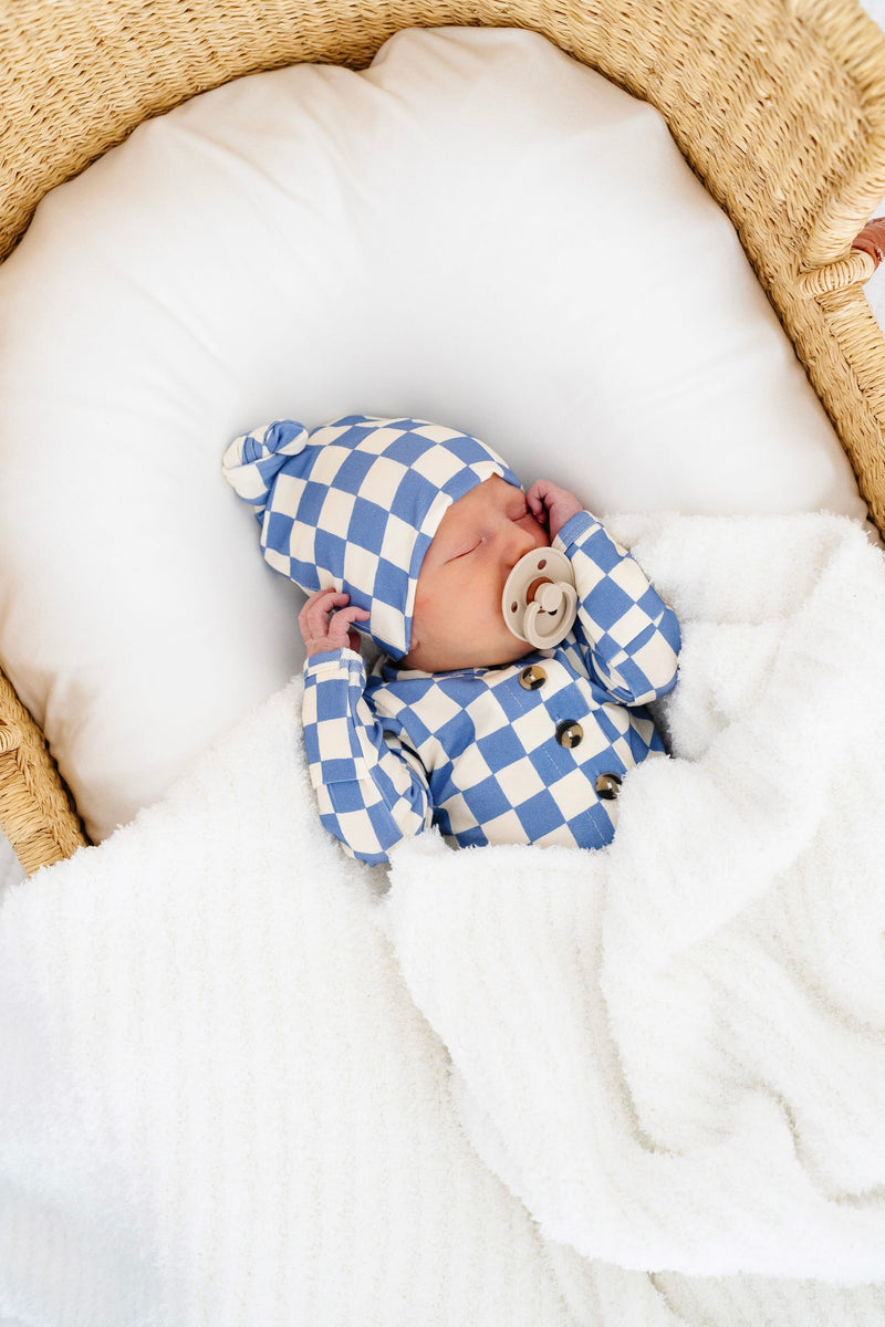 jett top and bottom newborn boy with matching jett top knot hat laying in bassinet with white chenille blanket