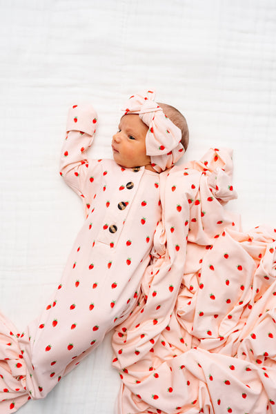 junie strawberry knotted gown and swaddle blanket. Newborn girl laying on bed with matching headband in junie