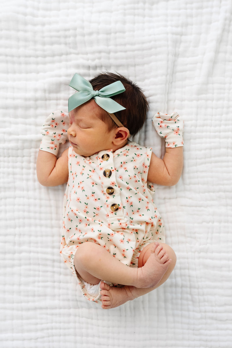 lottie bubble romper newborn girl laying on bed with mittens and sage satin bow