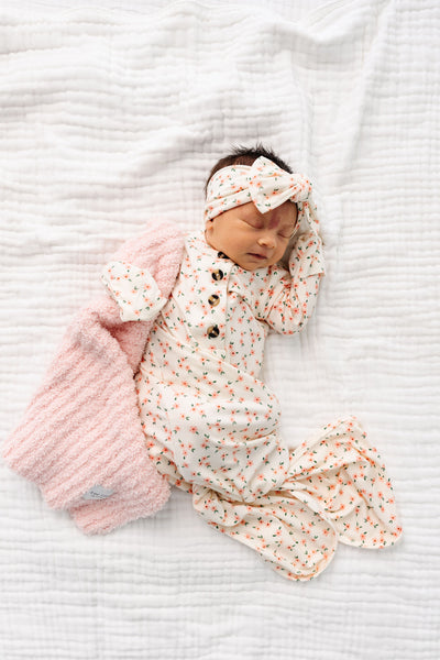 lottiel knotted gown newborn girl laying on bed with blush chenille mini with matching headband