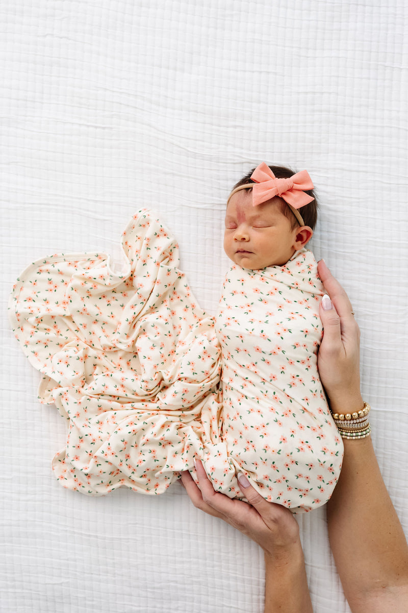 lottie swaddle blanket with matching mango linen bow newborn girl laying on bed.