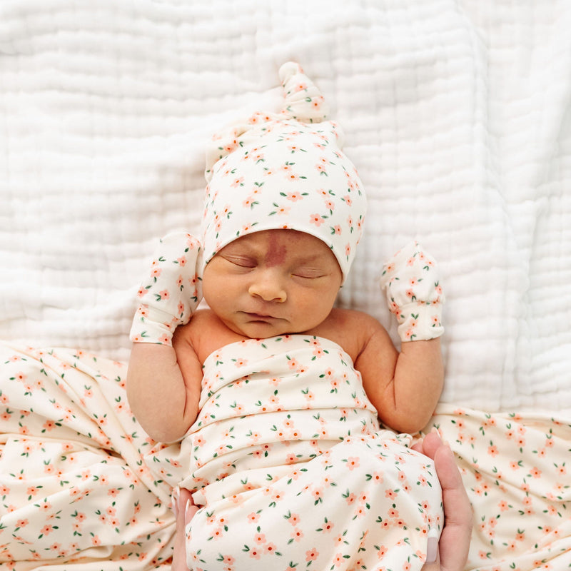 lottie top knot hat and hat bundle newborn girl laying on bed. mittens, top knot hat, and swaddle blanket.