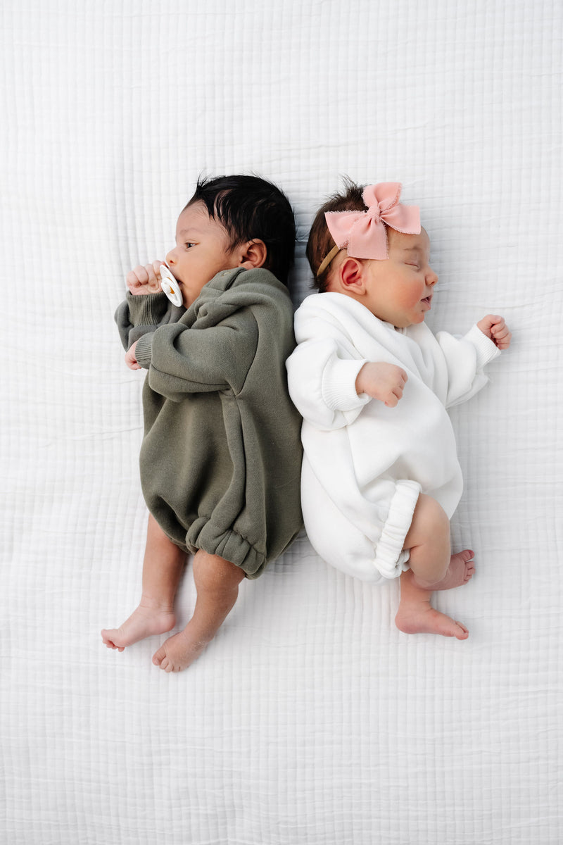 olive white sweatshirt romper baby girl baby boy laying on bed.