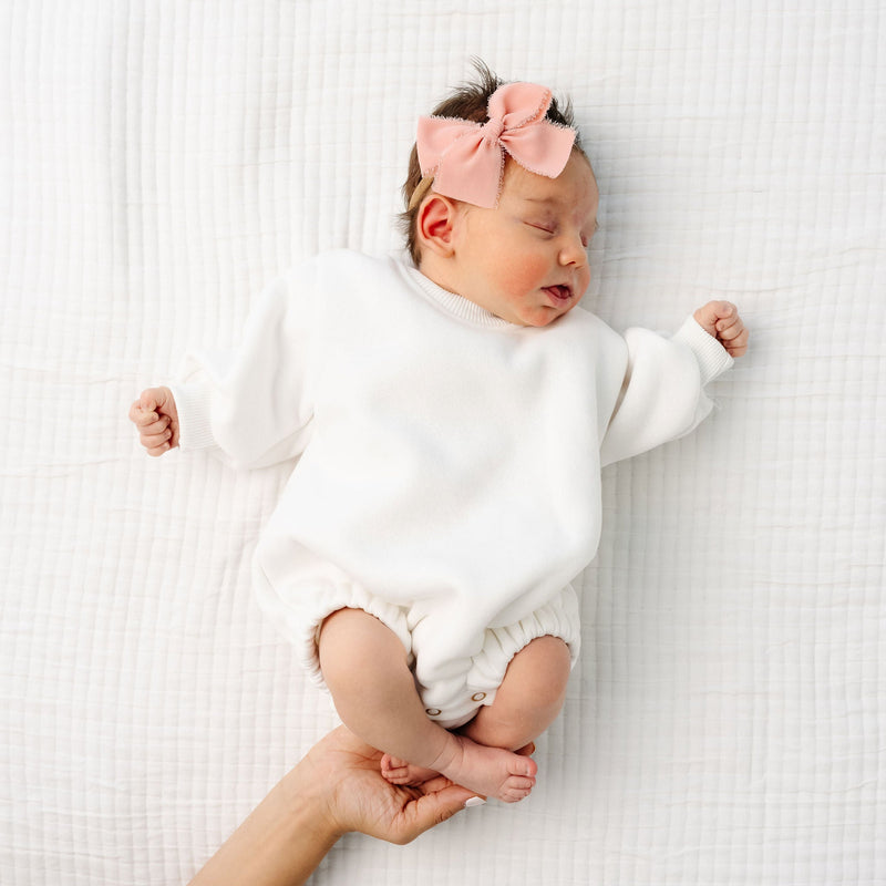 white sweatshirt romper baby girl laying on bed